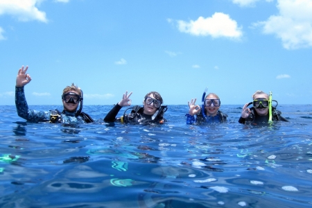 three introductory scuba divers and their instructor on the surface of the water after their dive posing with the OK sign