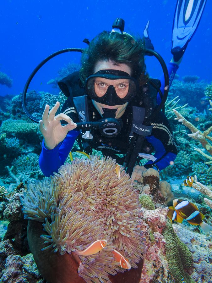 scuba diver posing behind anemone with ok hand sign